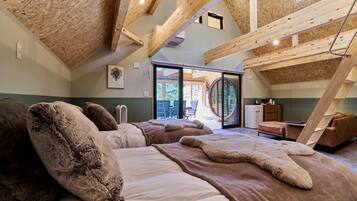 A spacious bedroom with a sloped ceiling, wooden beams, and a large bed with fluffy pillows.
