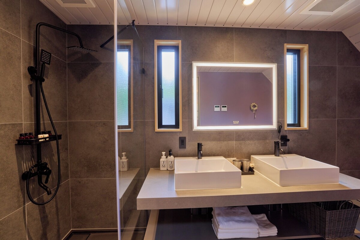 A modern bathroom with two sinks, a shower, and a large mirror.