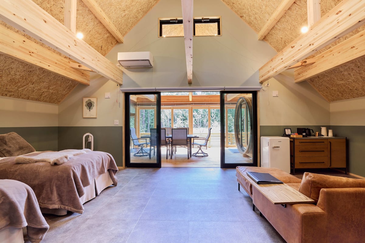 A room with a bed, a sofa, a table, and a view of an outdoor area with a table and chairs.