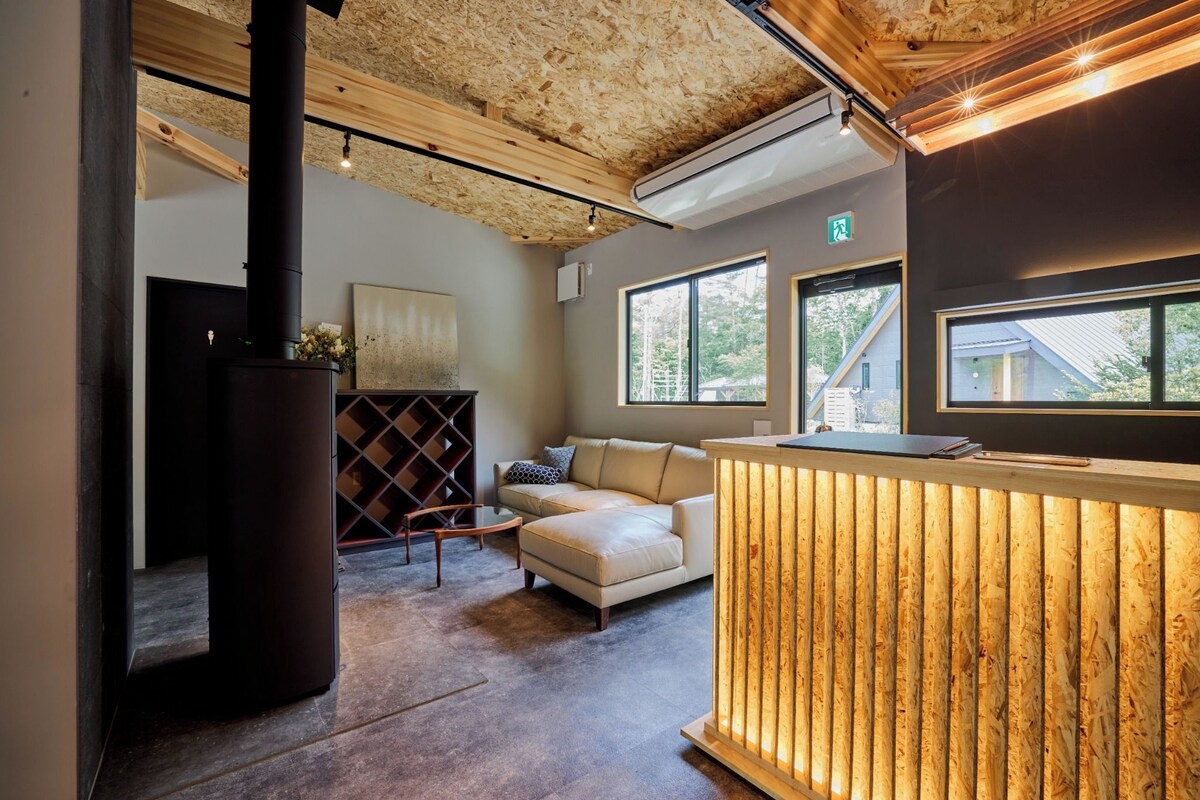Un interior moderno con chimenea, un sofá, un mostrador de recepción de madera y ventanas amplias.