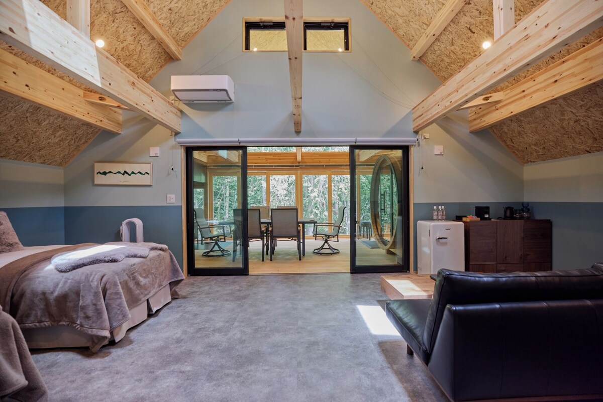 A bedroom with a bed, a desk, and a chair. There is a window and a door leading to a balcony.