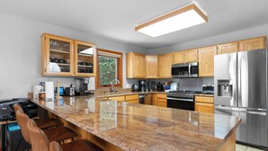 A modern kitchen with granite countertops, wooden cabinets, stainless steel appliances, and a bar area with stools.