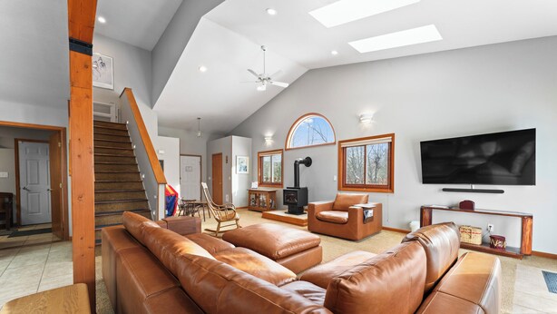 A spacious living room with a large brown leather sectional sofa, a wooden staircase, a flat-screen TV, and a fireplace.