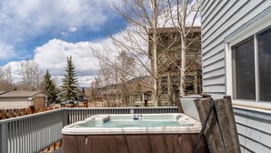 A hot tub on a deck with a wooden fence, a wooden bench, and a view of a house and trees.