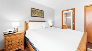 A neatly made bed with white linens, a wooden headboard, and a bedside table with a lamp and a clock.