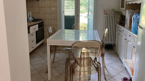 A kitchen with a dining table and chairs, a window with blinds, and a radiator. - Relaxation house (Marche)