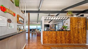 Un área de recepción moderna con un mostrador de madera, vista al océano, interior espacioso con piso de madera y un ventanal grande.