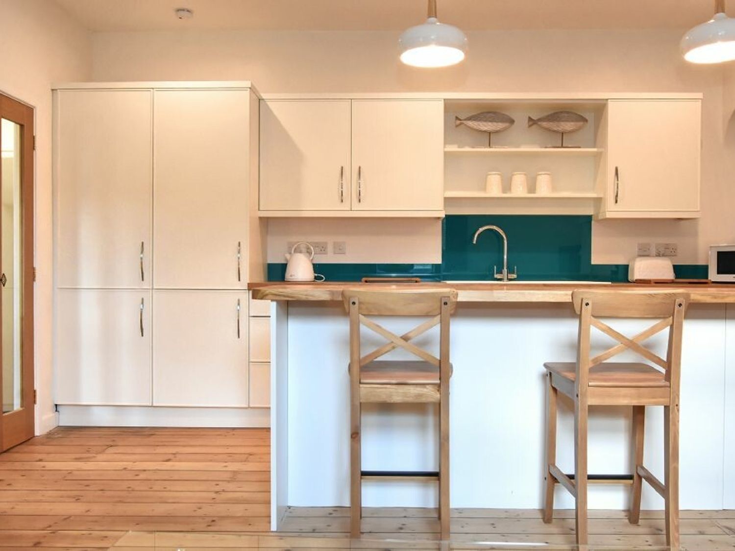 A modern kitchen with white cabinets, a teal backsplash, and wooden bar stools.