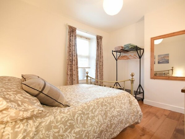 A bedroom with a bed, a window with curtains, a bedside table with a lamp, and a mirror on the wall.
