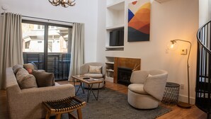 Ett modernt vardagsrum med en soffa, fåtöljer, ett soffbord, en öppen spis och ett stort fönster med gardiner.