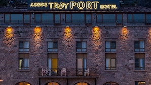The Assos Troy Port Hotel with a stone facade, outdoor seating, and boats docked in front. - Assos Troy Port Hotel (Ayvacik)