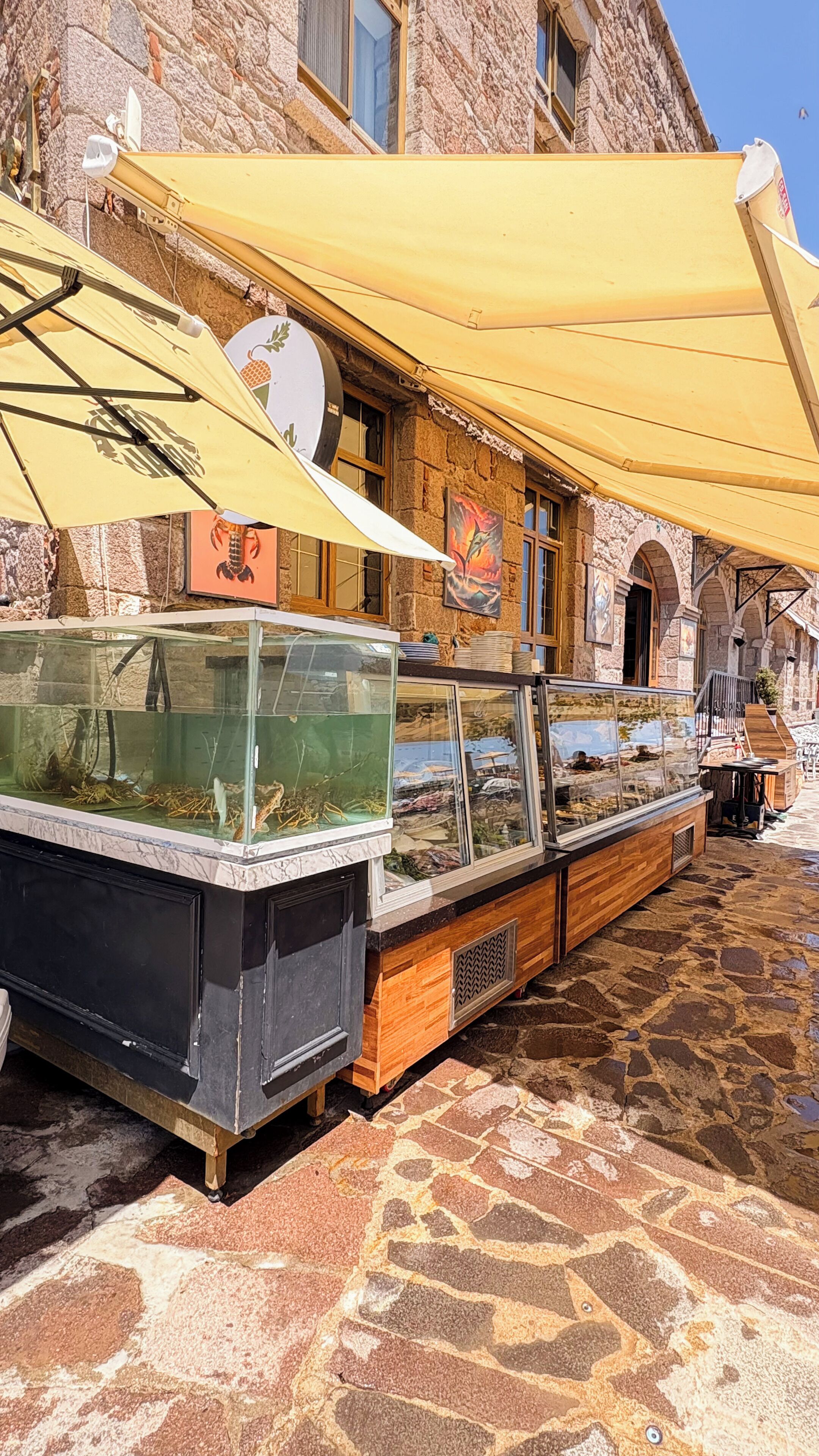 A seafood display with glass tanks, a stone building, and a yellow awning in the background.