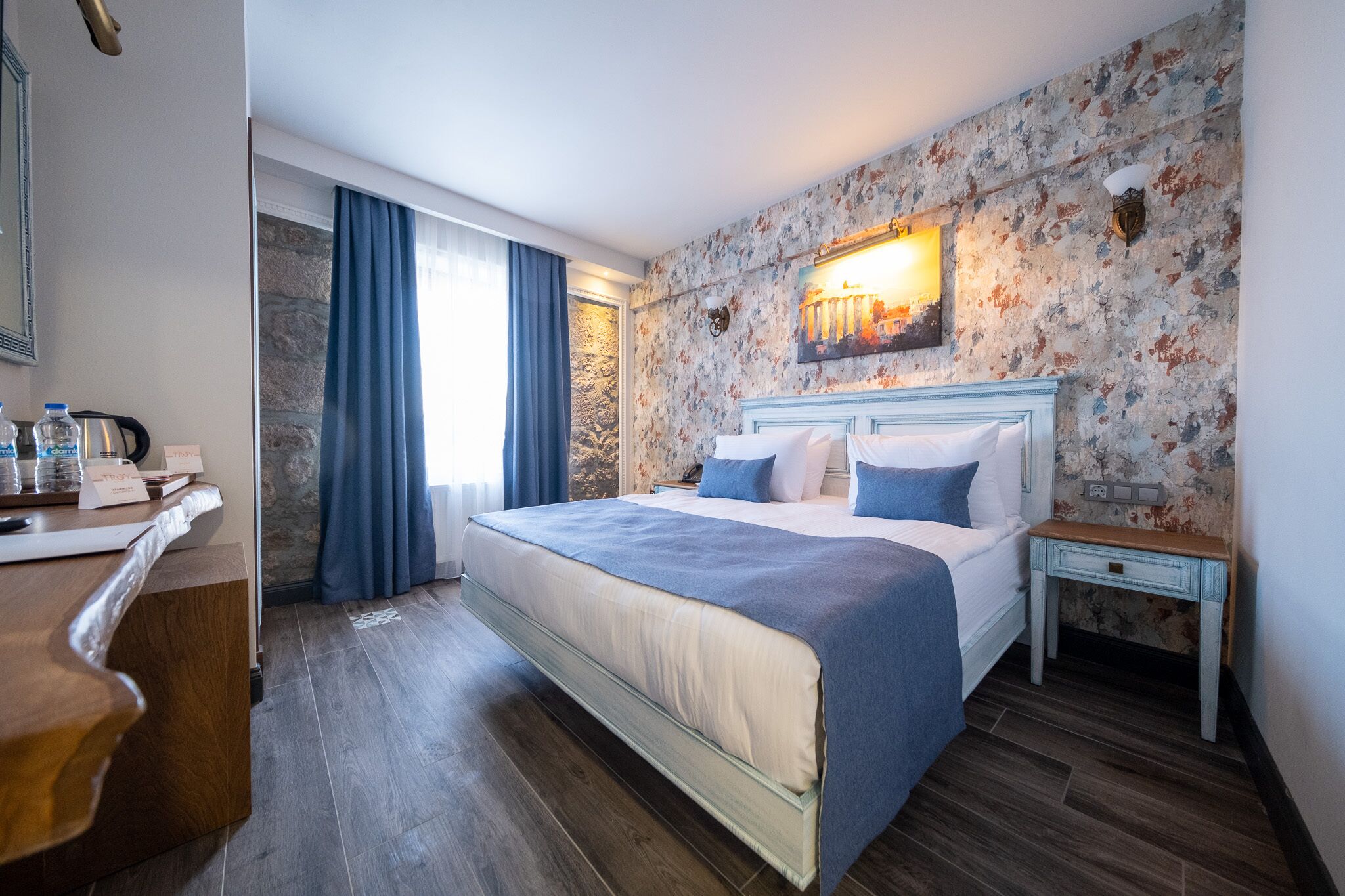 Et hotelværelse med en stor seng, et skrivebord med et spejl og en stenvæg.