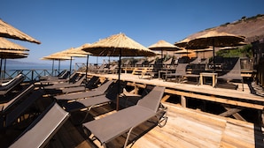 A beachside lounge area with sun loungers and thatched umbrellas, overlooking the sea. - Assos Troy Port Hotel (Ayvacik)