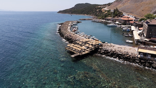 A coastal town with a rocky breakwater, clear blue sea, and boats docked. - Assos Troy Port Hotel (Ayvacik)