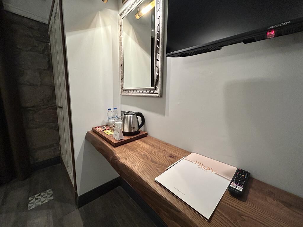 Habitación de hotel con una mesita de madera, un espejo, una tetera, un control remoto y una botella de agua.