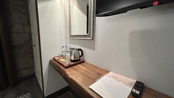 Habitación de hotel con una mesita de madera, un espejo, una tetera, un control remoto y una botella de agua.