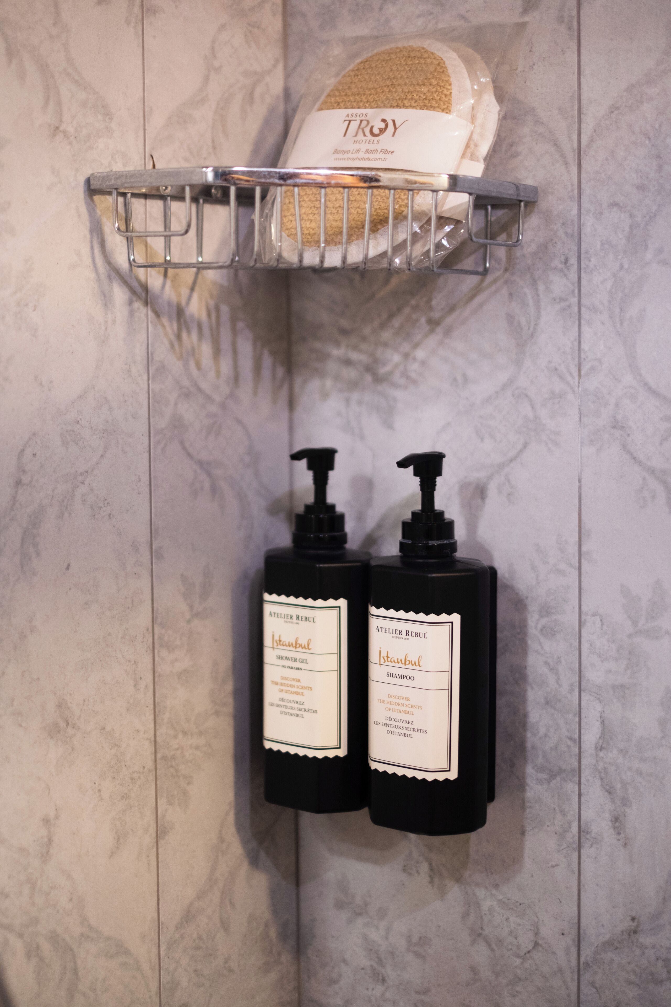 Un baño con zona de ducha, un perchero con toalla y dos botellas negras de gel de ducha y champú de Istanbul.