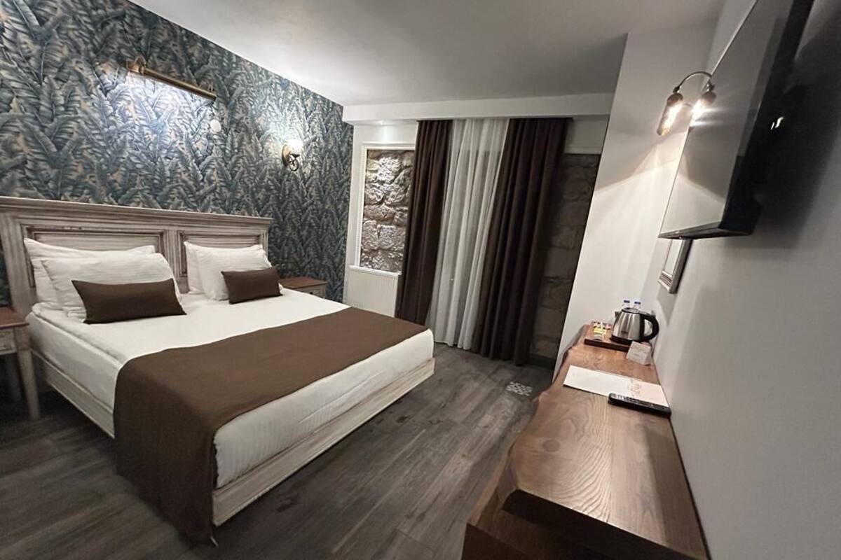 Une chambre d’hôtel avec un grand lit, un bureau en bois, un téléviseur à écran plat et un mur en pierre.