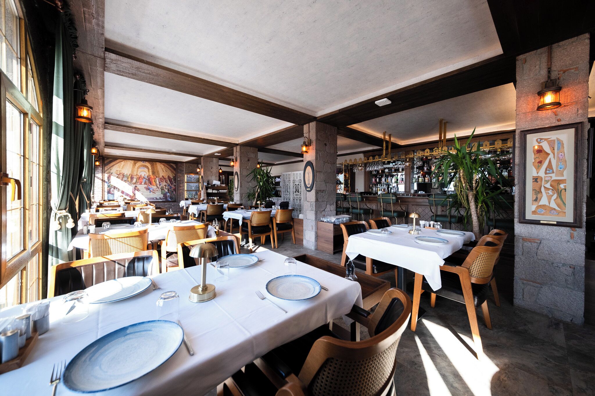 A restaurant with multiple tables set for dining, wooden chairs, and a bar area in the background.