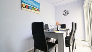 Ein Essbereich mit einem weißen Tisch, schwarzen Stühlen, einer Wanduhr und einem Bild von bunten Häusern.