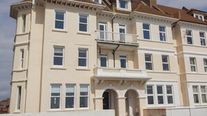 Ein mehrstöckiges Gebäude mit einer symmetrischen Fassade, großen Fenstern und einem zentralen Balkon.