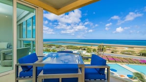 Un balcón con mesa de vidrio y sillas azules, con vista a una piscina y al océano.