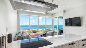 Una cocina moderna con un ventanal grande con vista al océano, un televisor de pantalla plana montado en la pared y una encimera elegante.