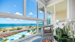 Habitación con una ventana grande que da a una piscina y al océano, un sofá gris y una orquídea en maceta.