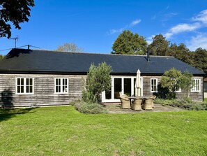 Une maison en bois avec un toit sombre, une véranda à l’avant avec des fauteuils en osier et une cour gazonnée.