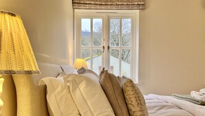 Ein ordentlich bezogenes Bett mit Lampe, Kissen und Blick auf eine verschneite Landschaft durch ein Fenster.