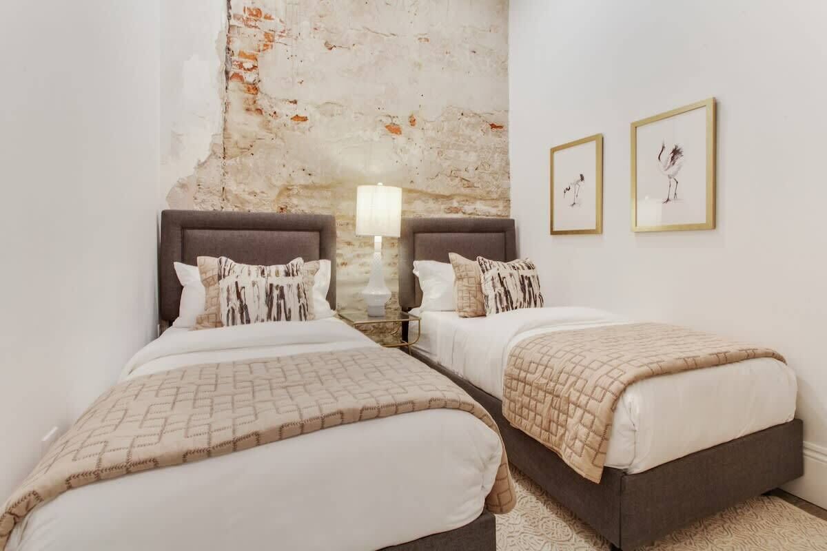 A double bed room with a rustic brick wall, two bedside tables with lamps, and framed artwork on the wall.