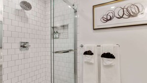 Ein modernes Badezimmer mit weißen Fliesen, einer Duschkabine aus Glas und zwei weißen Handtüchern mit braunen Akzenten.