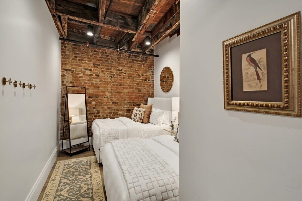 A room with two beds, a brick wall, a wooden ceiling, a framed picture, and a mirror.