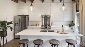 Une cuisine moderne avec des meubles blancs, des appareils en acier inoxydable et un îlot central doté de tabourets.