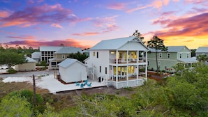 A two-story house with a balcony, surrounded by other houses and vegetation.