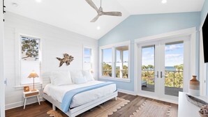 A bedroom with a bed, a ceiling fan, a window with a view, and a door leading to a balcony.