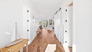 A bright hallway with white walls and wooden flooring, leading to a seating area with a sofa and a table.