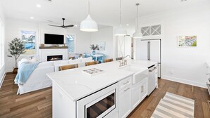 A modern kitchen with white cabinetry, a central island, and a dining area with blue chairs.