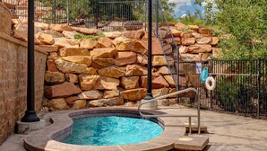 Ein Pool mit Steinmauer und Metallzaun in einer sonnigen Außenanlage.