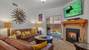 Ein Wohnzimmer mit einem braunen Ledersofa, einem Glastisch, einem Kamin und einem an der Wand montierten Fernseher.