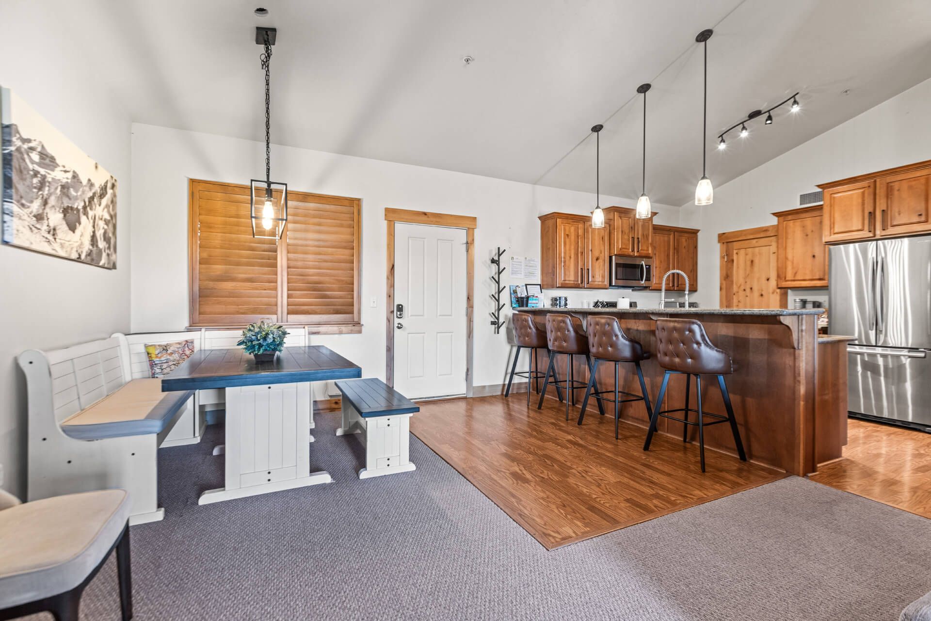 A modern kitchen with wooden cabinets, a stainless steel refrigerator, and a bar area with stools.