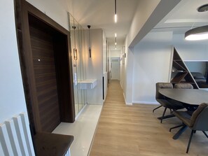 Un intérieur moderne avec un plancher en bois, un coin repas doté d’une table ronde et de chaises, et un couloir agrémenté d’un mur miroir et de luminaires suspendus.