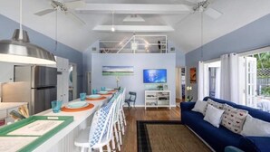 A modern kitchen with a dining area, a blue sofa, and a ceiling fan.