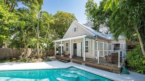 A house with a swimming pool, surrounded by lush greenery and a wooden deck.