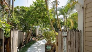 A narrow pathway flanked by wooden fences and lush greenery, leading to a house with a sign reading "Elizabeth's Secret."