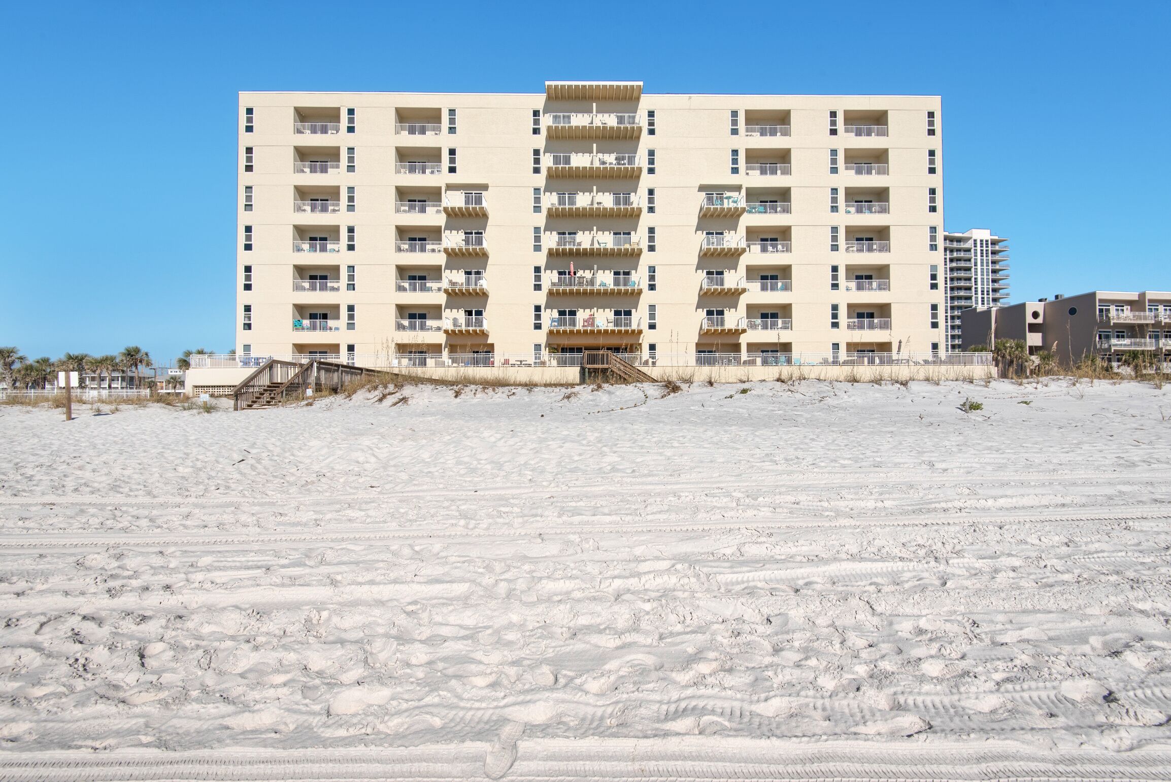 A multi-story hotel with balconies, located on a sandy beach.