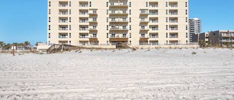 A multi-story hotel with balconies, located on a sandy beach.