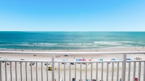Une vue sur la plage avec une balustrade blanche, des parasols de plage et un ciel dégagé.