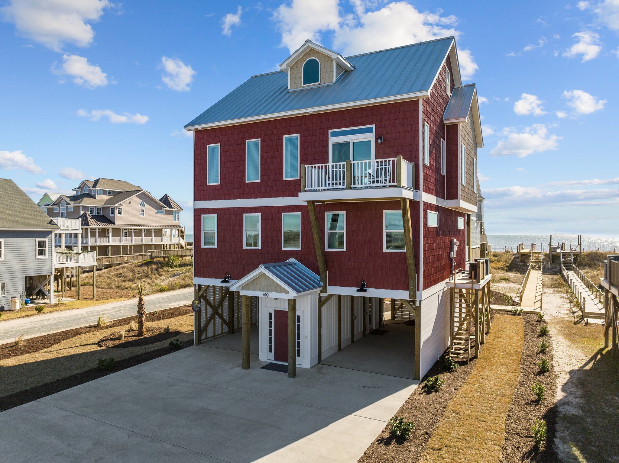 A multi-story house with a balcony on the second floor, a covered entryway, and a view of the beach.